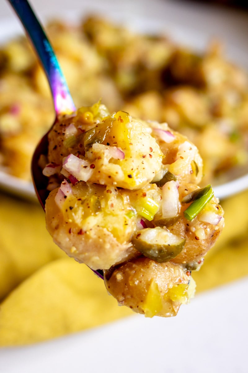 a rainbow spoon holding a scoop of dill pickle potato salad. 