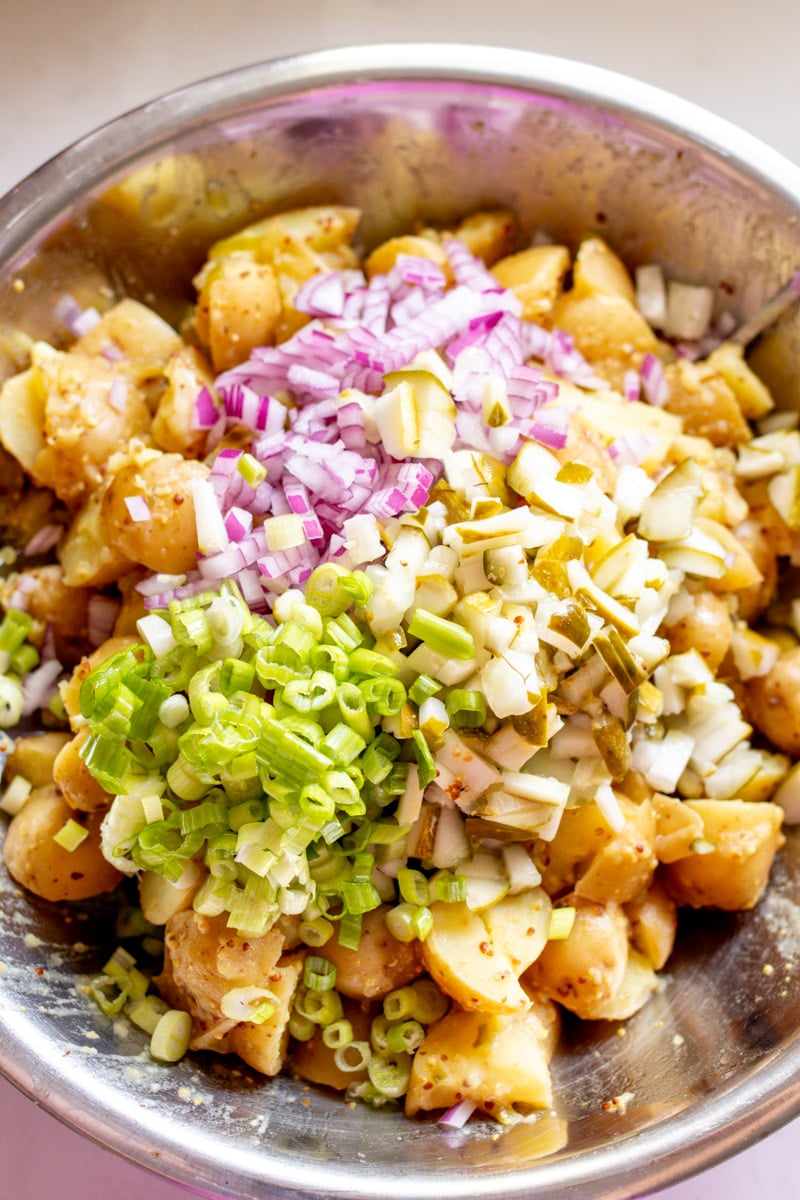 dill pickles, red onion, and scallions on top of a bowl of potato salad.