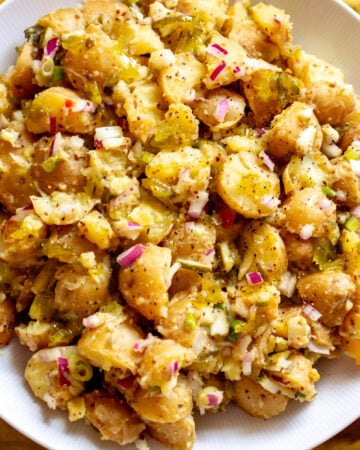 overhead view of a bright yellow dill pickle potato salad in a white bowl.