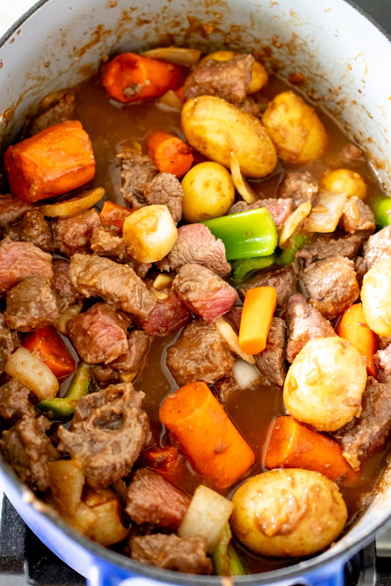 a dutch oven filled with broth and beef and vegetables.