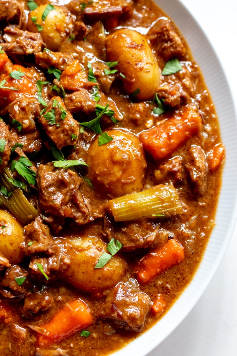 an up close view of the right side of a white bowl full of beef stew.