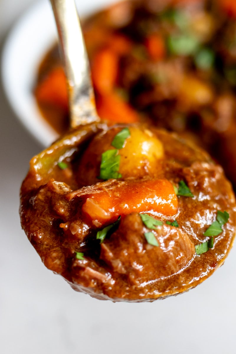 a ladle holding a scoop of tender beef and hearty vegetables.