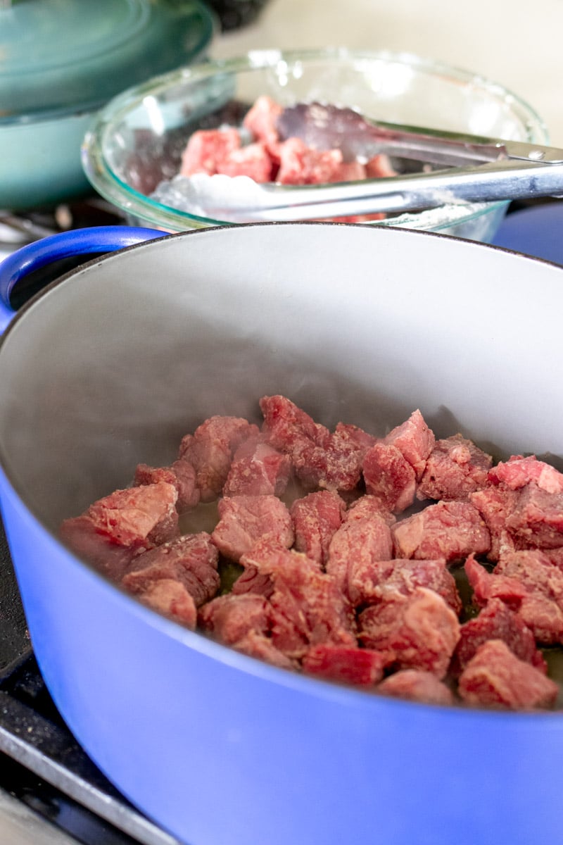 chunks of beef cooking in a dutch oven.