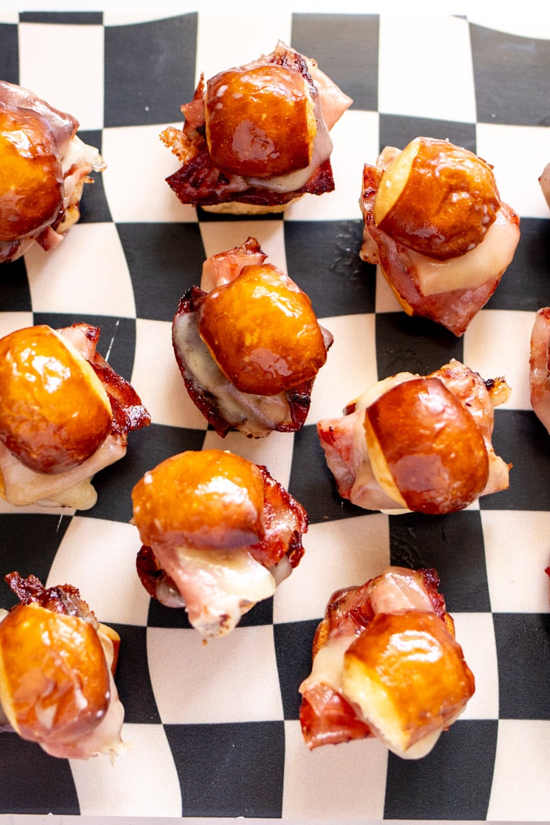 an overhead view of a cutting board full of pretzel bun sliders filled with mortadella and cheese.