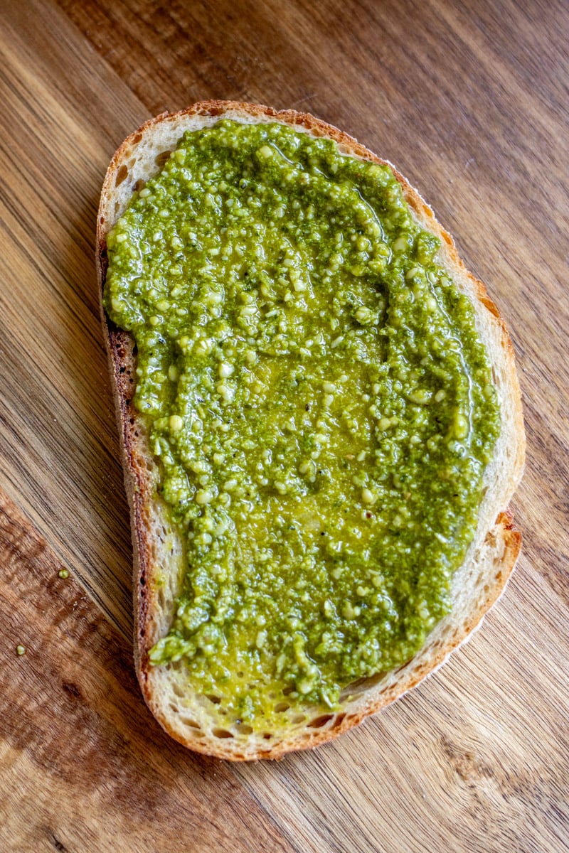 a piece of bread with green pesto smeared onto it. 