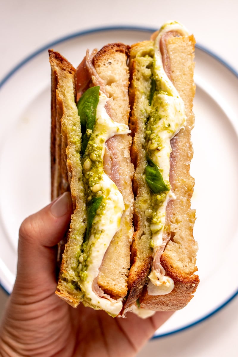 two hands holding two halves of a grilled cheese with pesto and mozzarella.