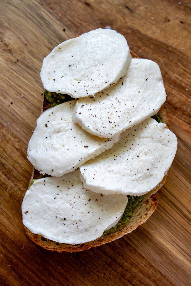 mozzarella cheese on top of a pesto smeared piece of bread.