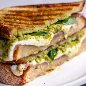 a panini cut in half showing the interior of melted mozzarella, prosciutto and pesto.