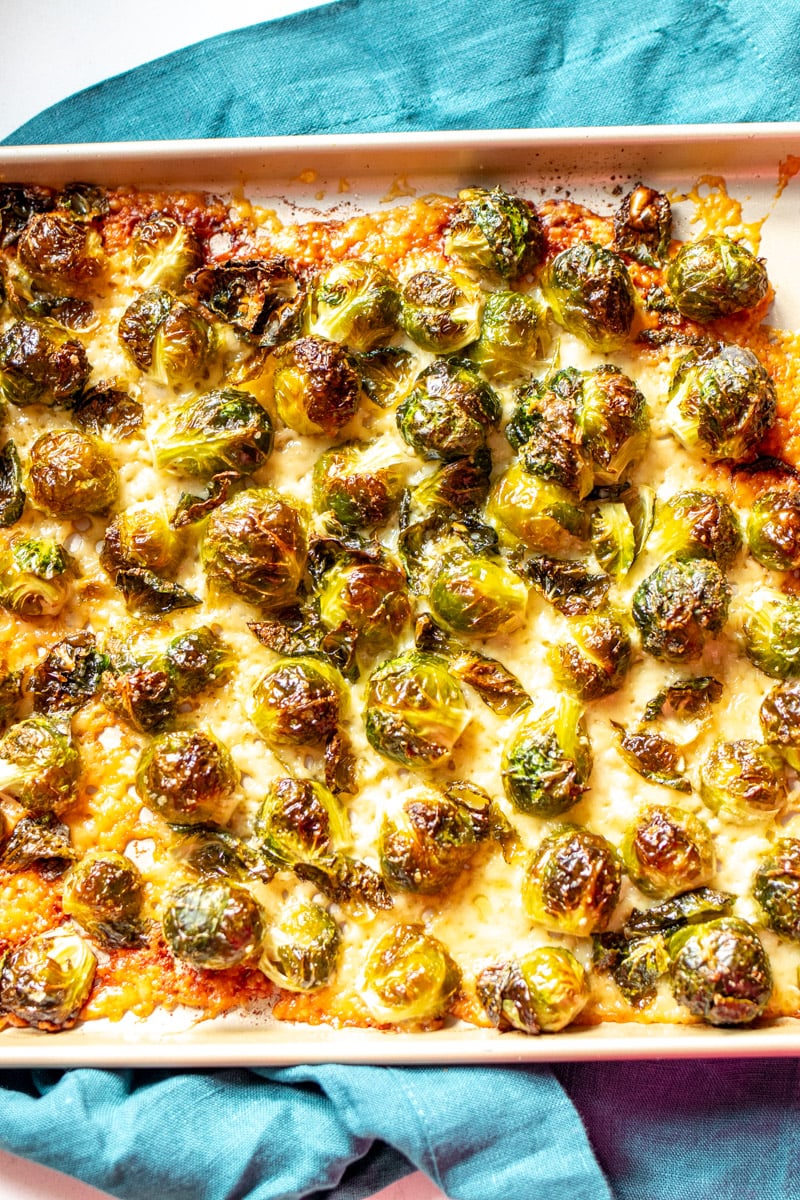 a sheet pan full. of parmesan crusted brussels sprouts with a blue towel underneath.