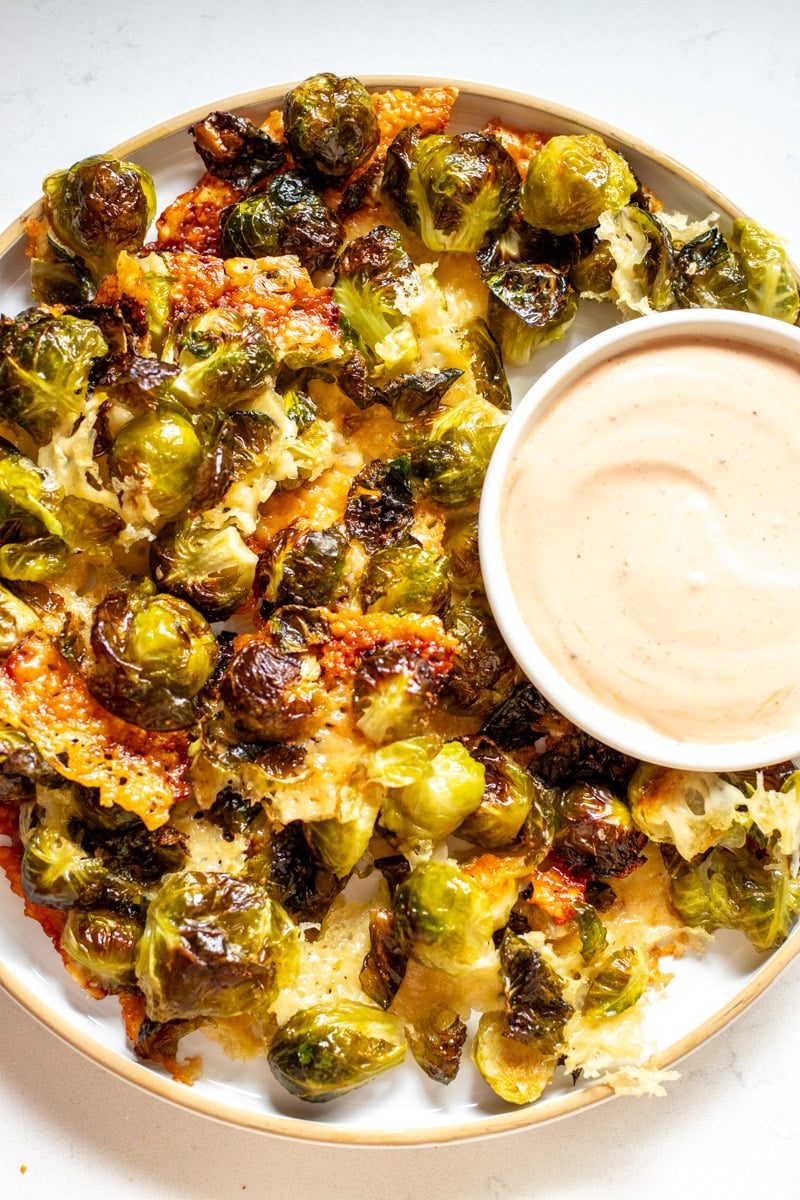 crispy cheesy brussels sprouts on a plate with dipping sauce.