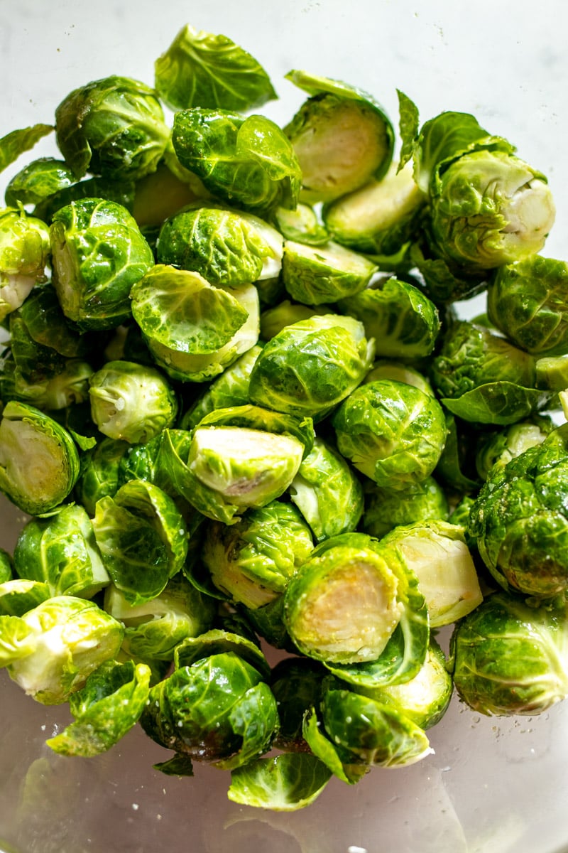 halved brussels sprouts tossed in olive oil, salt and garlic powder in a glass bowl.