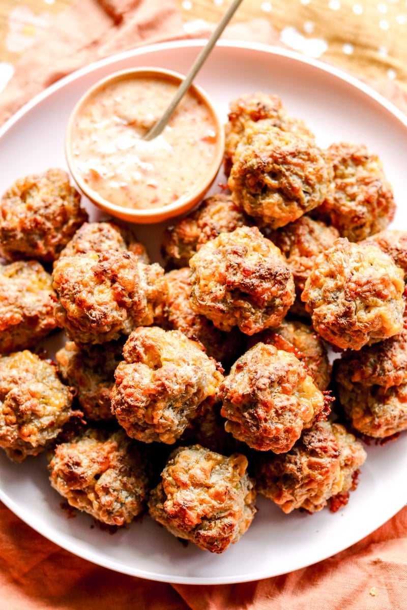 a pink plate full of brown sausage balls with a cream colored dipping sauce.