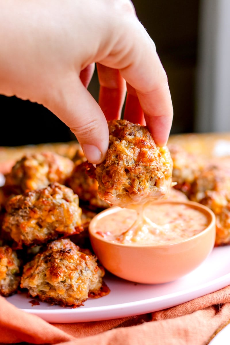 a hand dunking a sausage ball into dip.