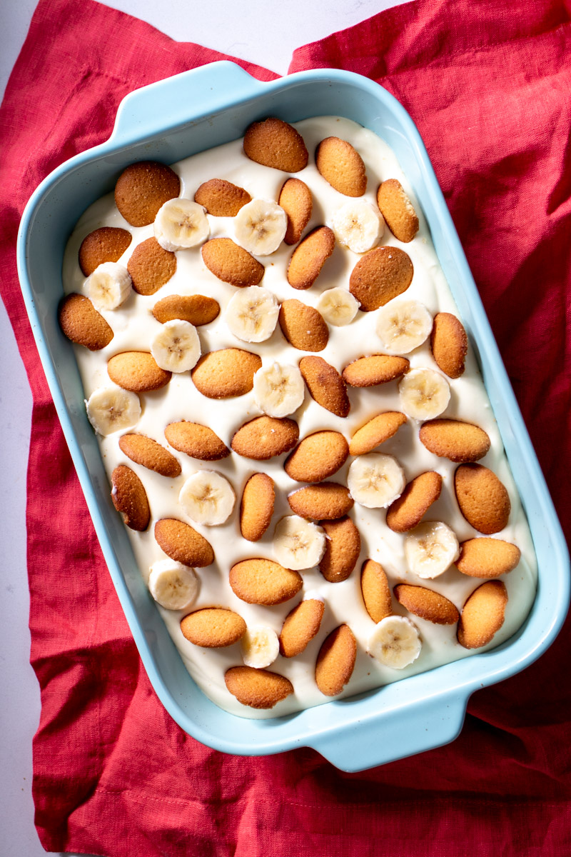 an entire  dish of southern banana pudding in a blue bowl over a pink napkin.