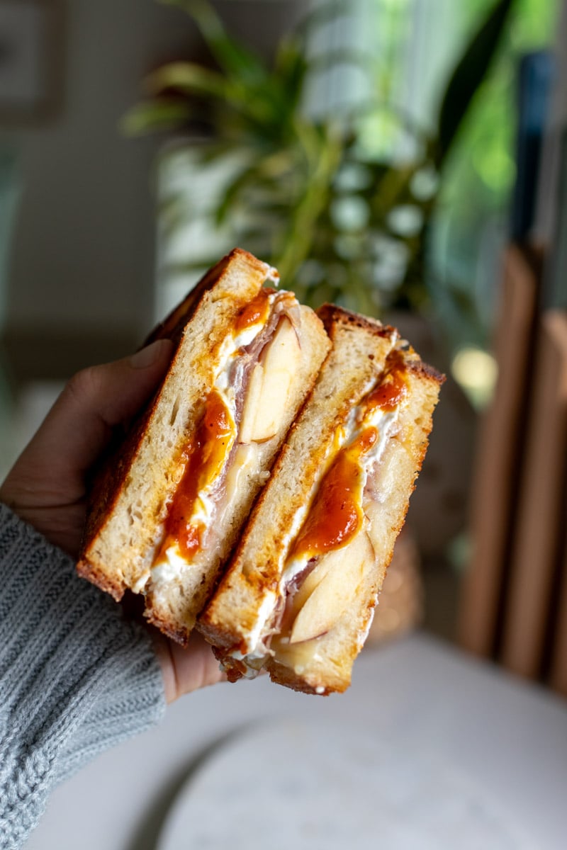 a hand holding up a halved pumpkin butter grilled cheese sandwich.