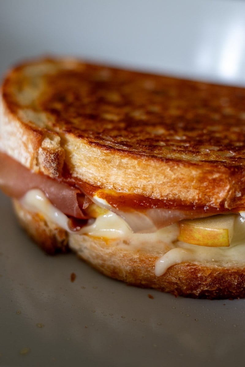 a grilled cheese sandwich getting all melty  in a white frying pan. 