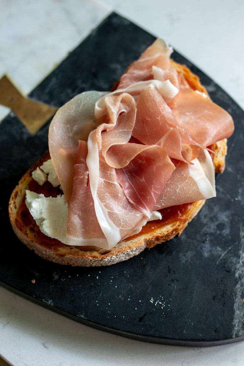 prosciutto slices on a piece of bread with trader joe's pumpkin butter and goat cheese.