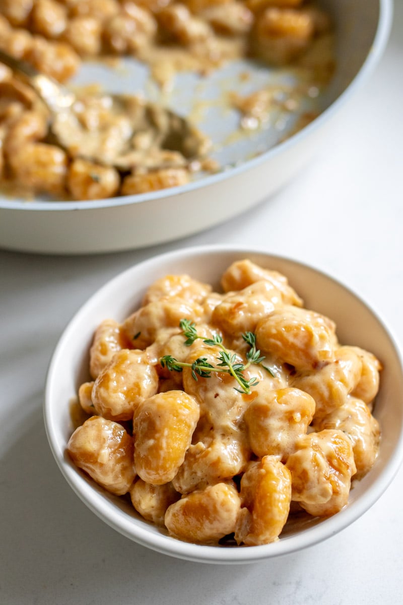 a small serving bowl filled with pumpkin gnocchi in a creamy sauce with the serving pan behind it.