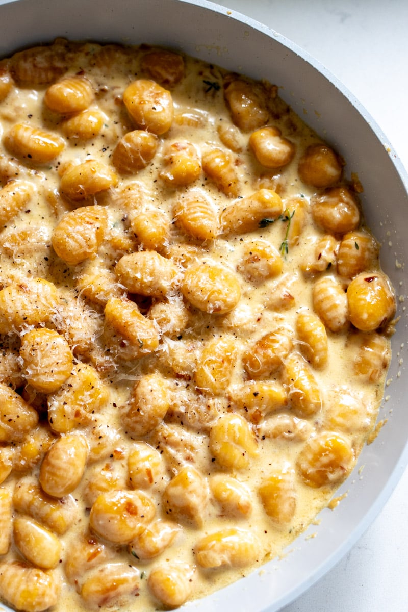 the right side of a skillet full of creamy sauce and trader joe's pumpkin gnocchi.