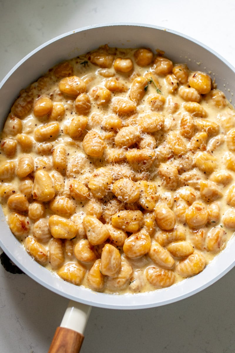 a large skillet filled with pumpkin gnocchi in a creamy sauce.