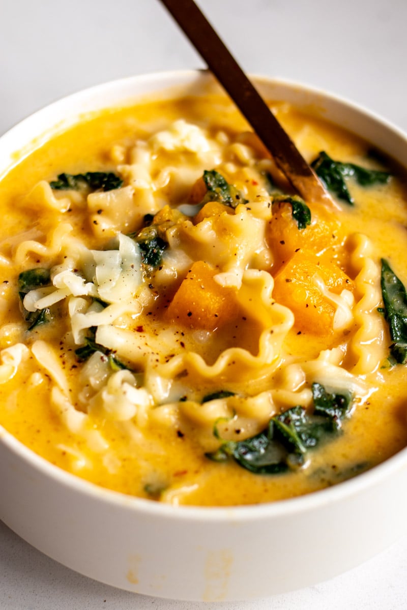 a white bowl filled with bright orange butternut squash lasagna soup.