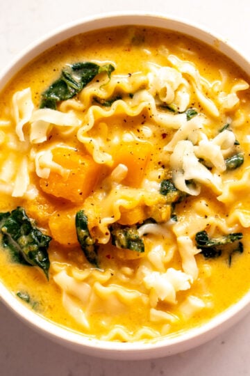 an overhead view of a bowl of butternut squash lasagna soup with kale and mozzarella cheese.