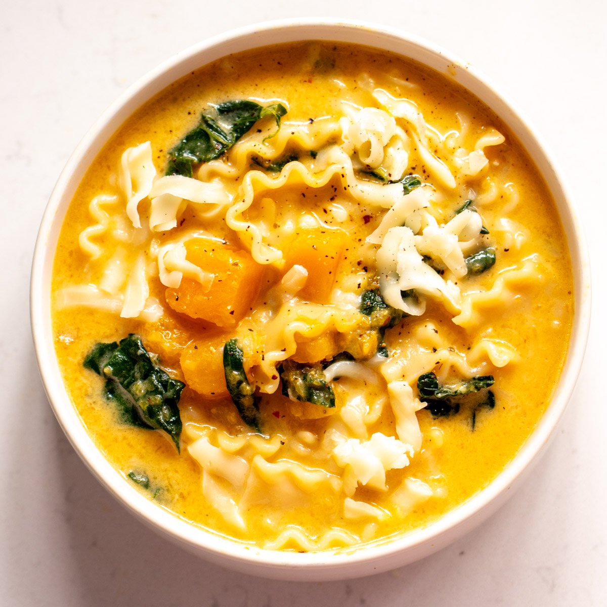 an overhead view of a bowl of butternut squash lasagna soup with kale and mozzarella cheese.