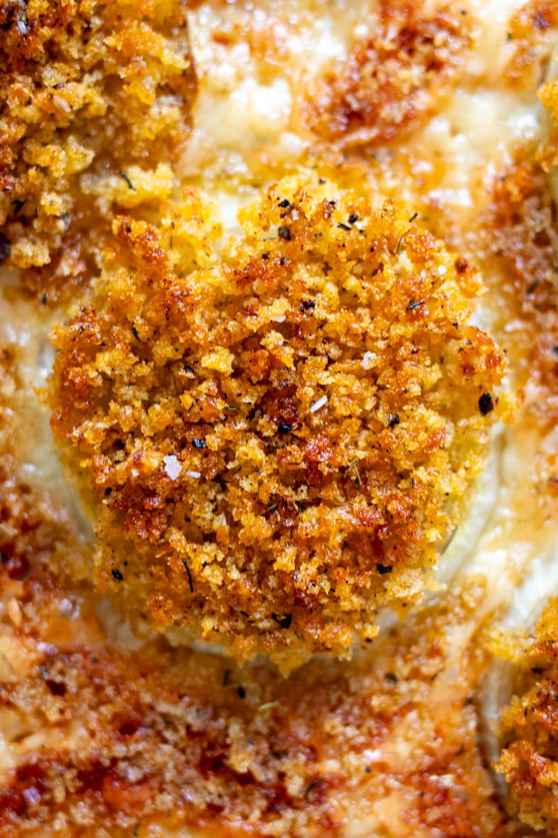 an up close view of one single bloomin onion bite on a baking sheet with lots of crispy cheese around the corners. 