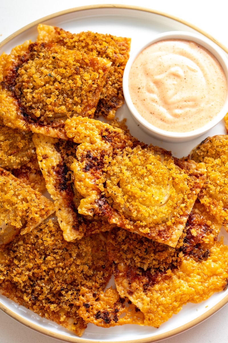 a white plate filled with crispy onion bites with a orange dipping sauce. 