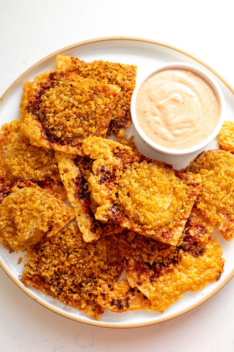 a white plate filled with gruyere crusted onion bites and bloomin onion sauce.