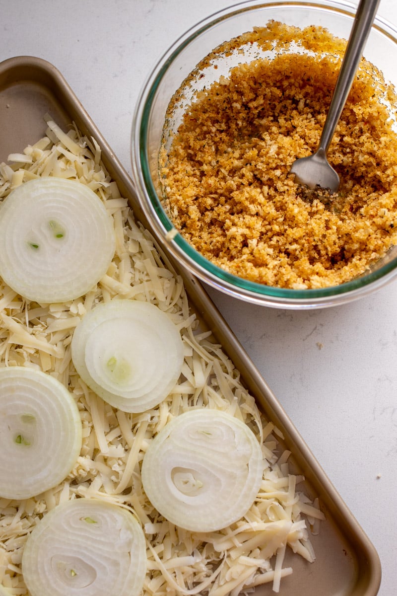 a baking sheet lined with cheese and onions and a small glass bowl full of crunchy bits.