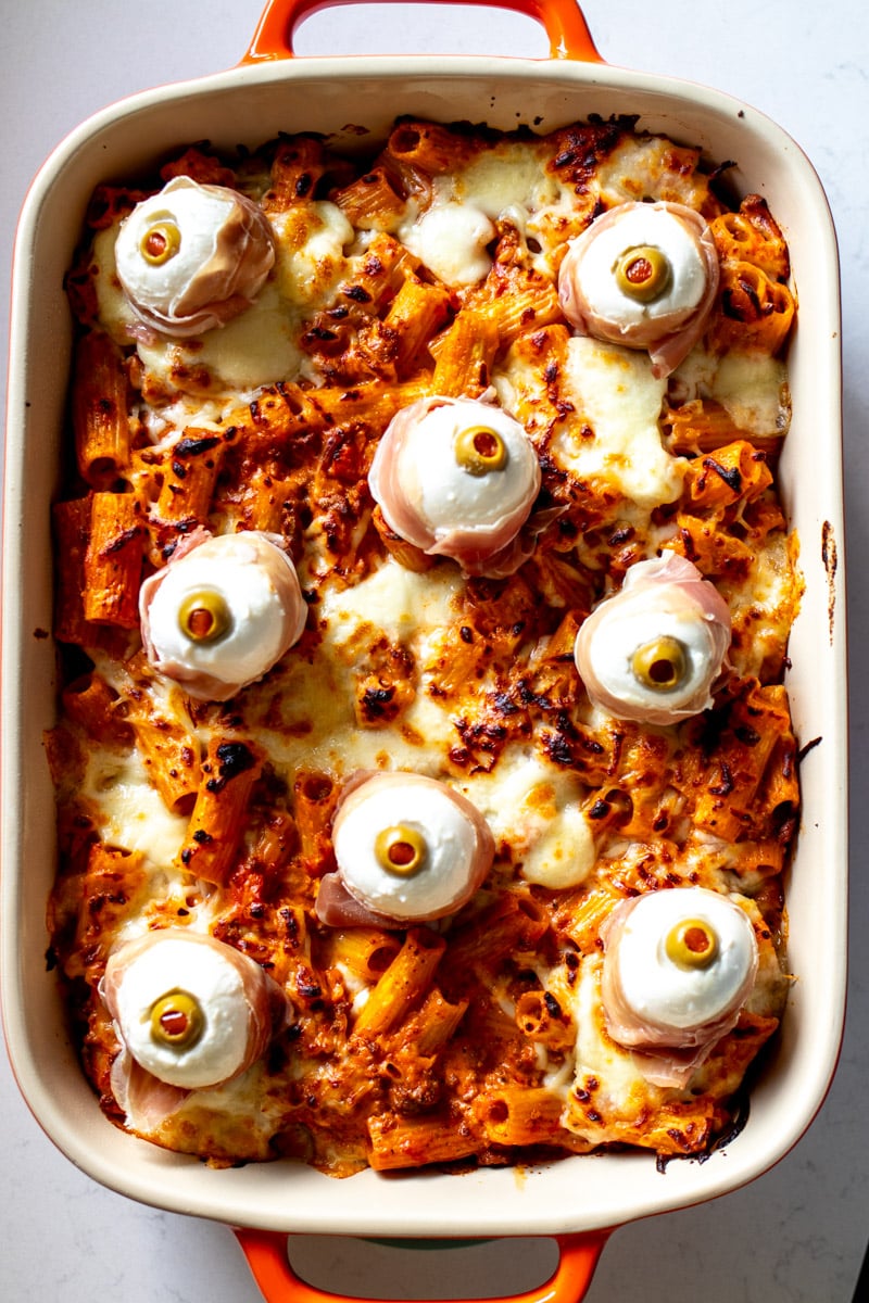 a large orange baking dish full of spooky halloween pasta - a baked ziti with eyeballs on it.