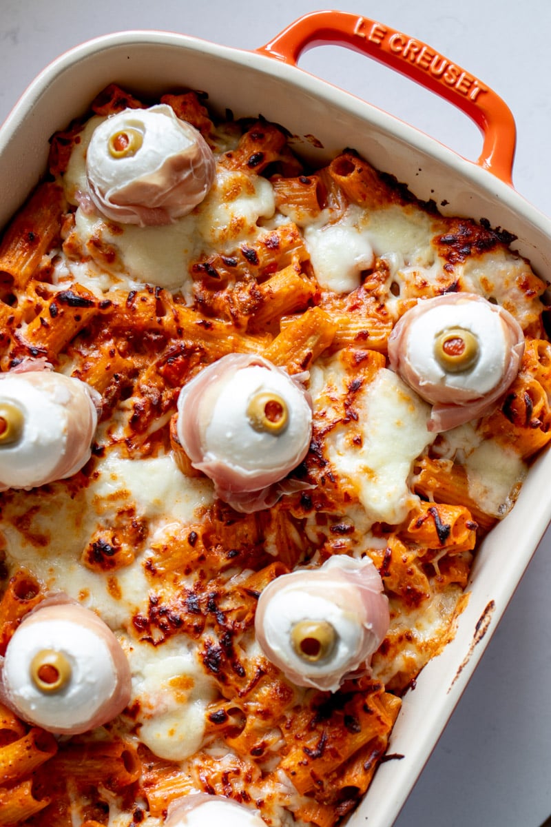 the upper right side of a orange baking dish full of baked ziti with mozzarella eyeballs.