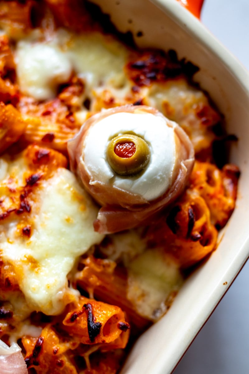 a single spooky mozzarella eyeball on a baking dish full of baked ziti.