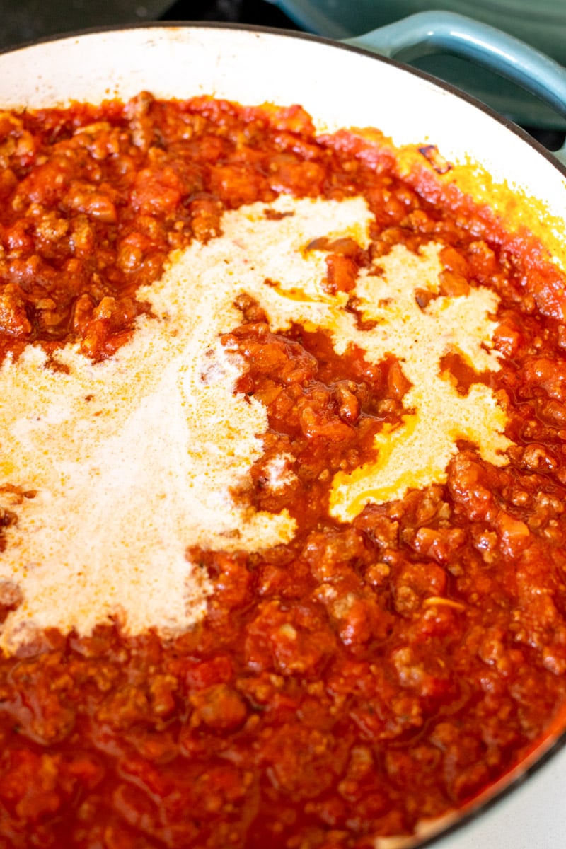 tomato sauce with heavy cream being poured into it.