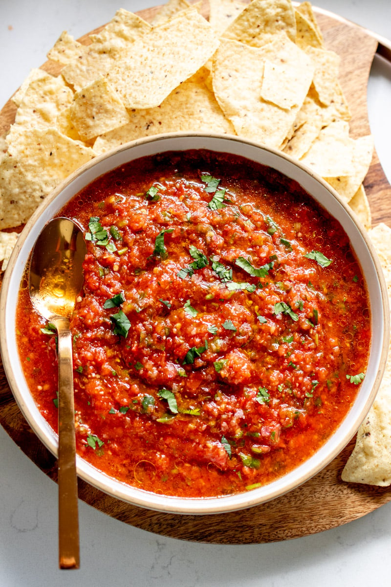 a bowl of bright red hot salsa next to a stack of tortilla chips.