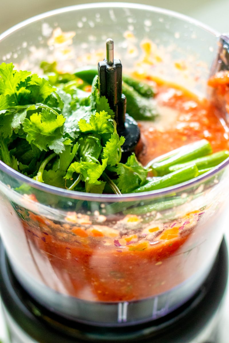 hot peppers on the top of a food processor with red chunky fresh salsa underneath.