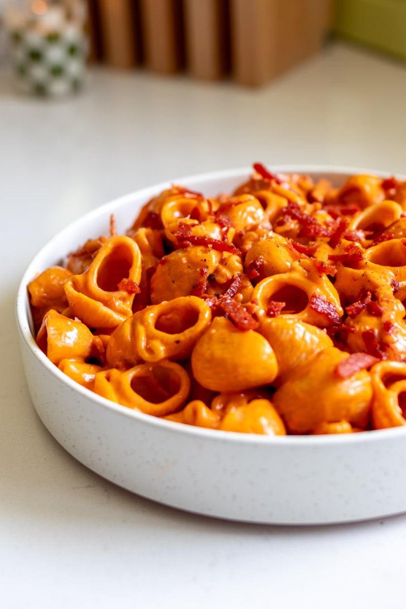 a white plate on a white countertop full of bright orange pasta.