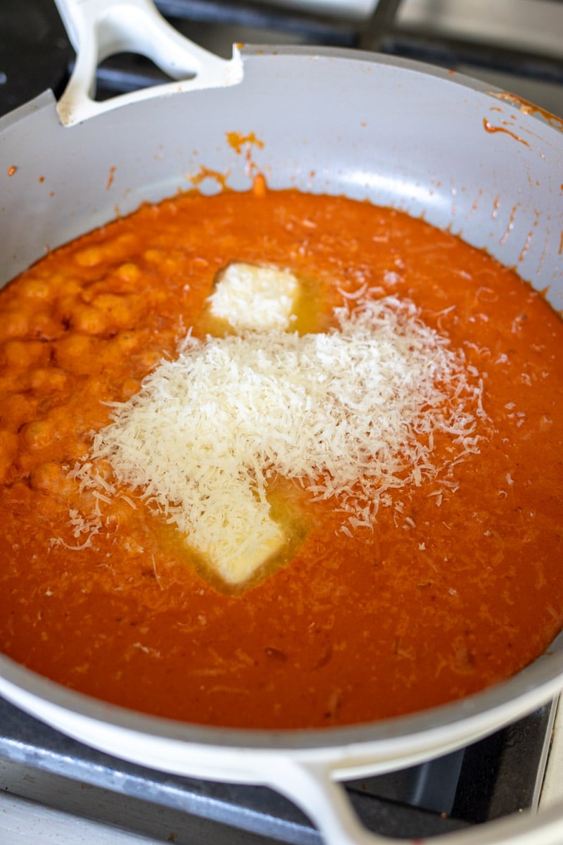 cheese, butter and milk being stirred into a pot of pasta sauce. 