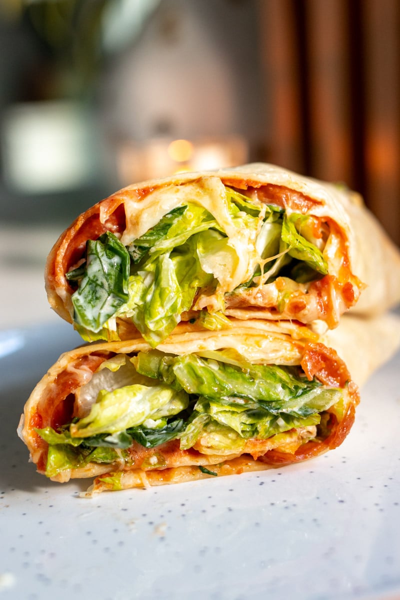 a pepperoni pizza caesar salad wrap on a white plate.