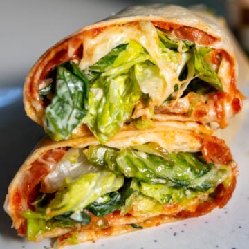 two halves of a pepperoni pizza caesar salad wrap on a white plate - showing the inside of the wrap.