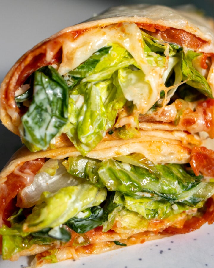 two halves of a pepperoni pizza caesar salad wrap on a white plate - showing the inside of the wrap.