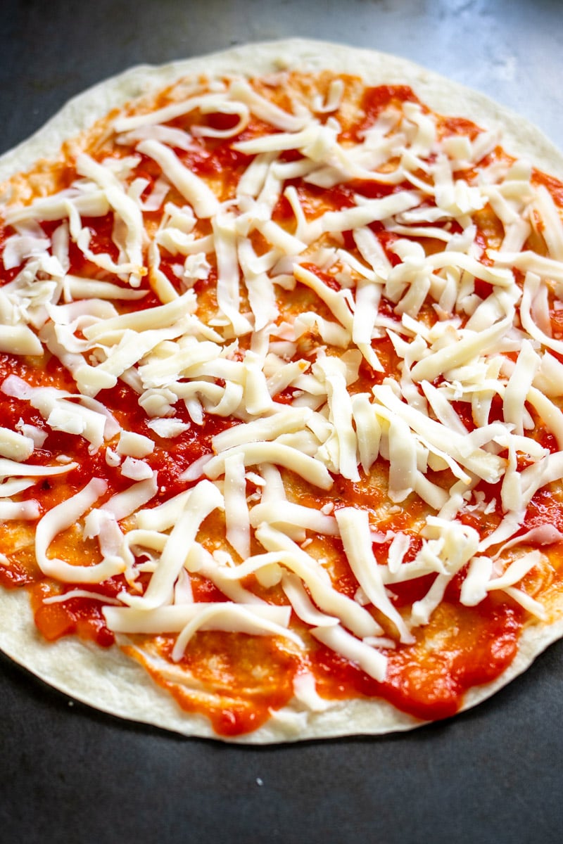 a tortilla pizza on a black baking sheet.