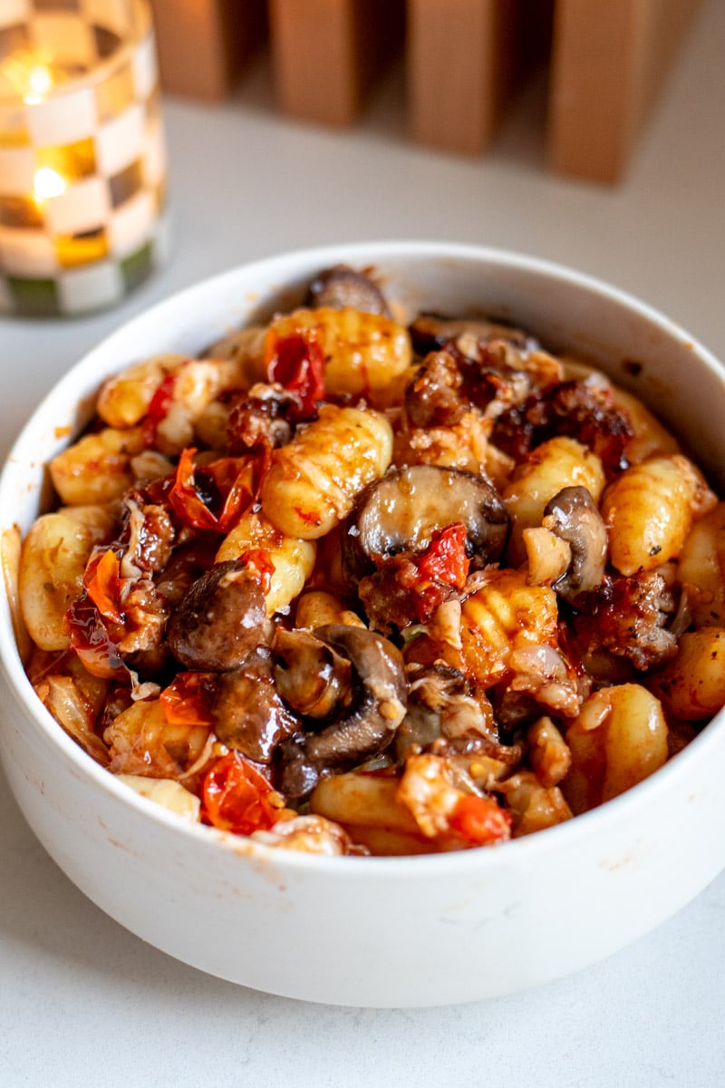 a white bowl full of sheet pan sausage, veggies, and gnocchi