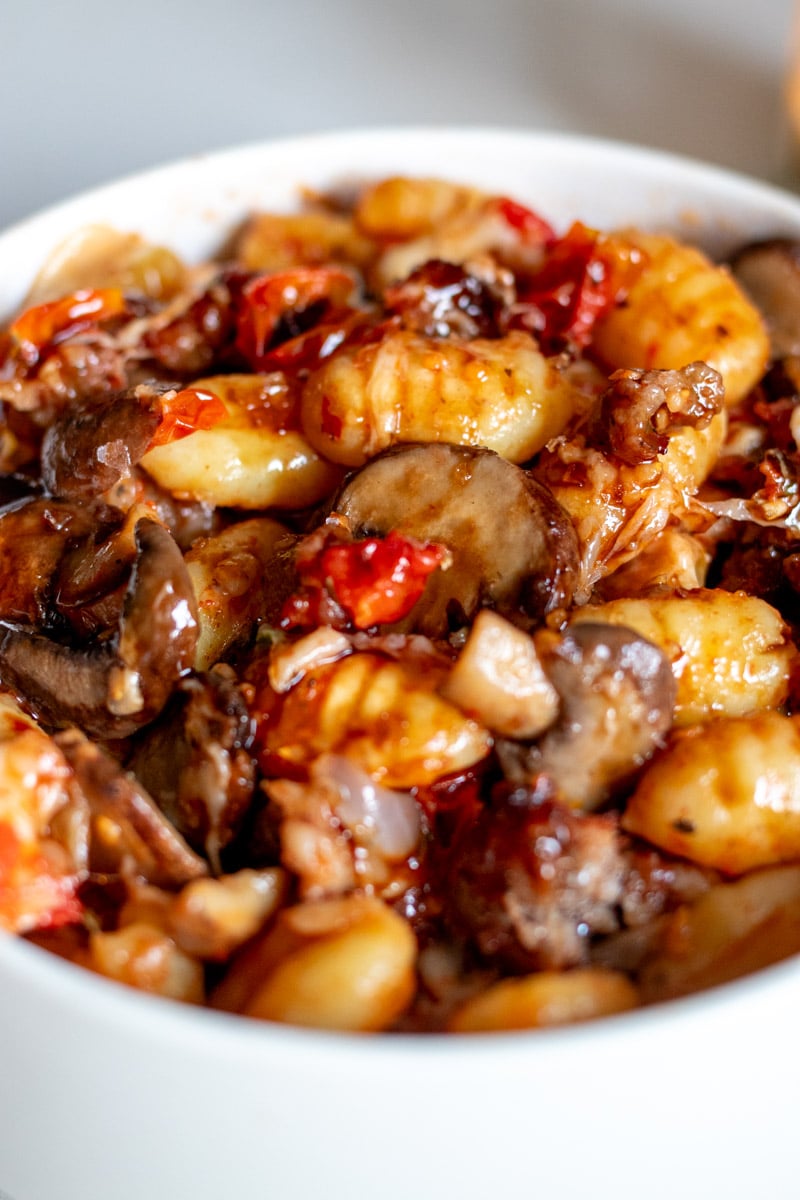 an overhead view of a white bowl filled with sausage, gnocchi and veggies and cheese.