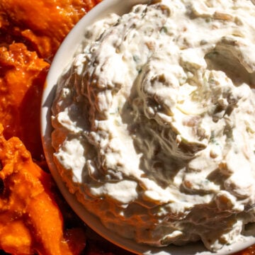 caramelized onion dip in a white bowl with orange buffalo wings next to it.