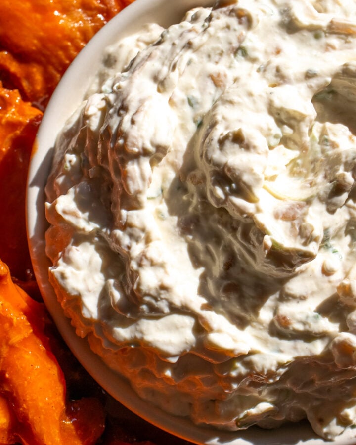 caramelized onion dip in a white bowl with orange buffalo wings next to it.