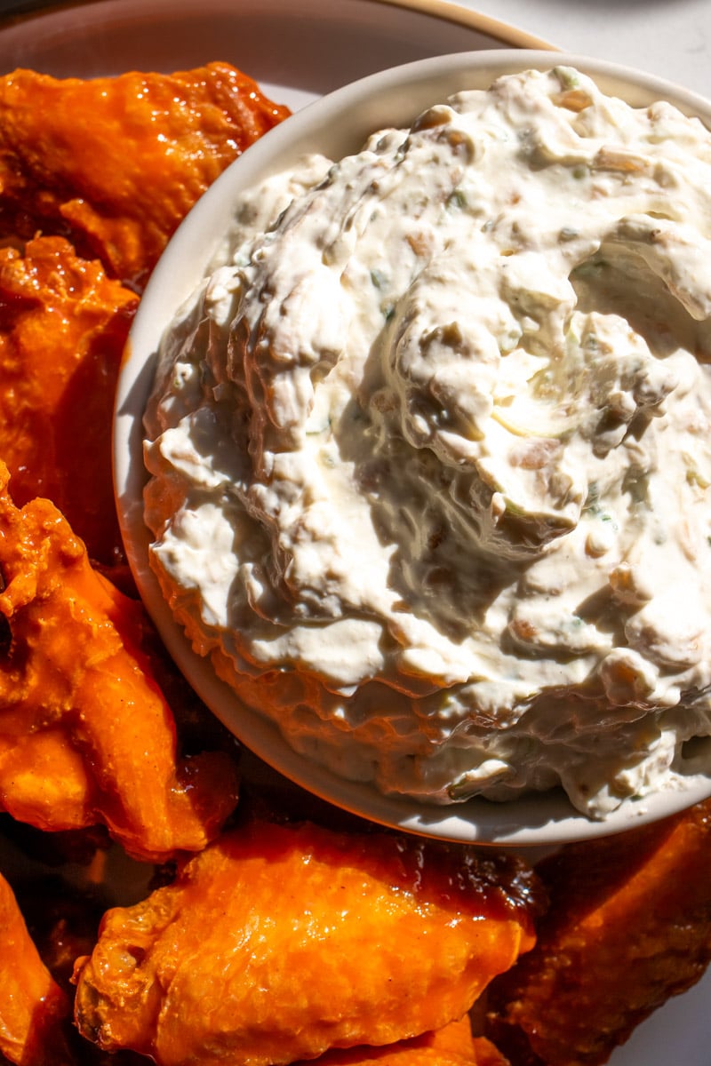 caramelized onion dip in a white bowl with orange buffalo wings next to it. 