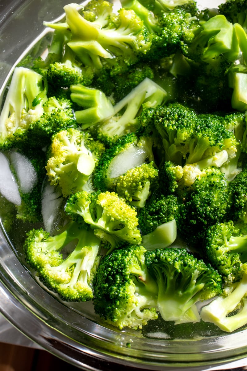 a glass bowl full of ice water and broccoli florets.