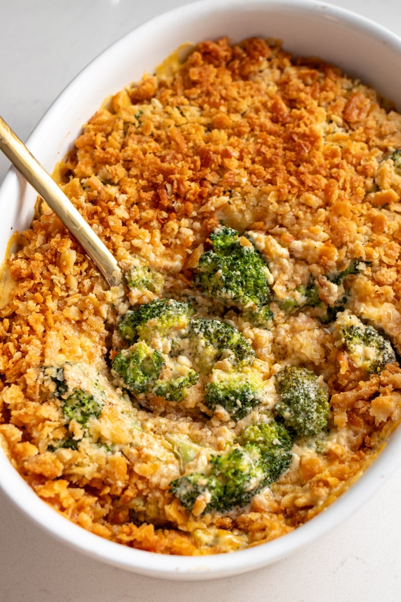 cheesy broccoli casserole in a white baking dish with a golden spoon. 